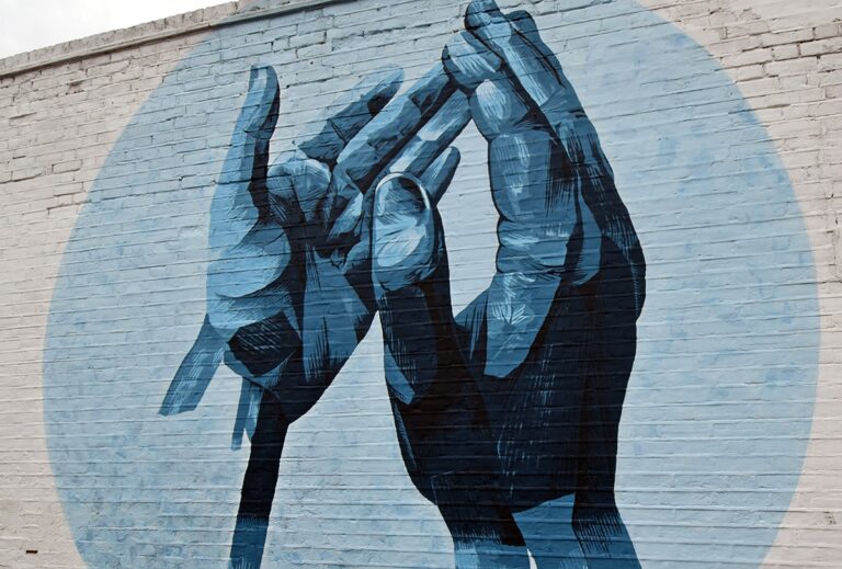 Mural on a brick wall—two clapping hands in a light blue circle
