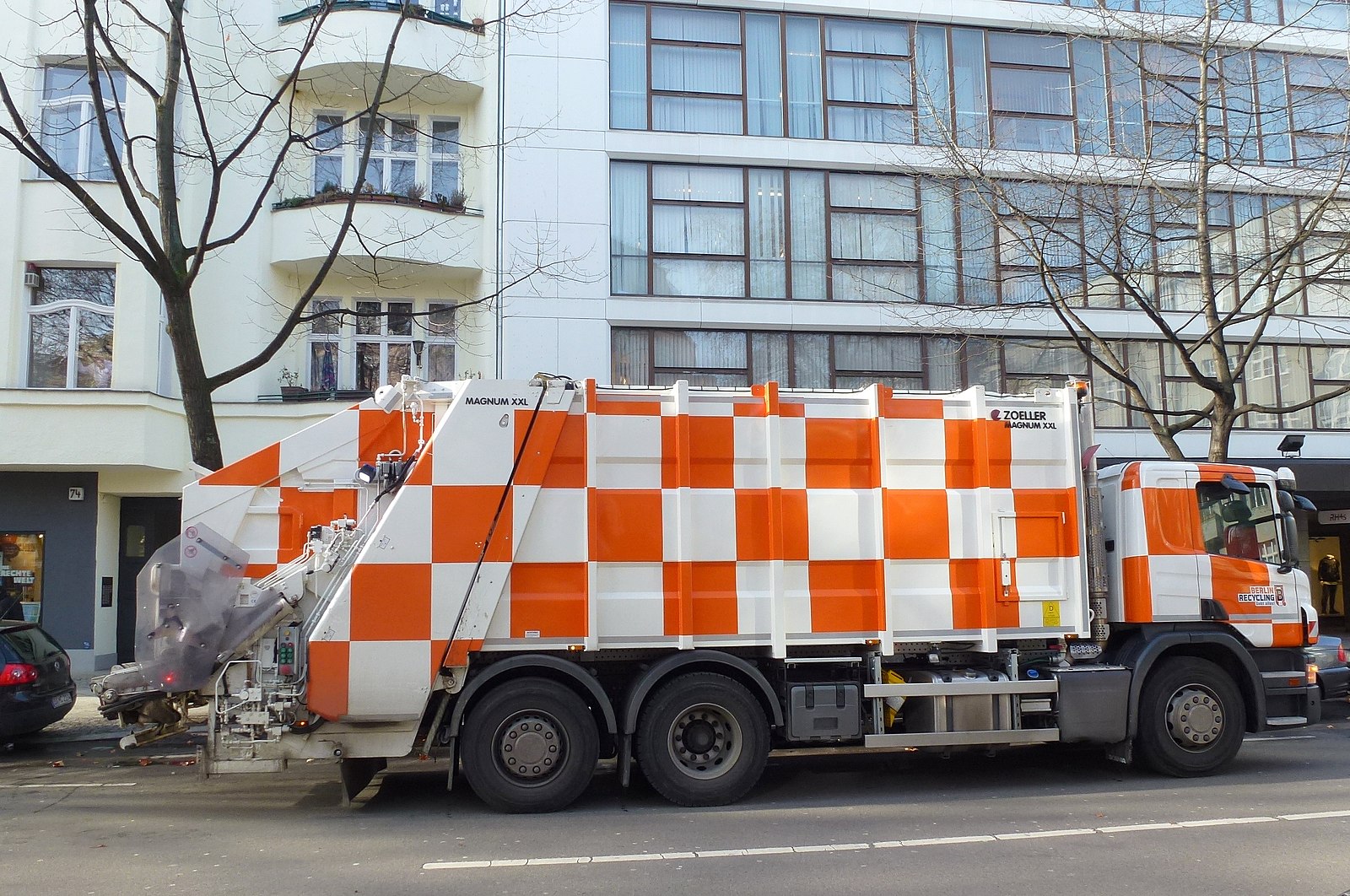 Orange-and-white checkered recycling truck in front of an apartment building on a street in Berlin.