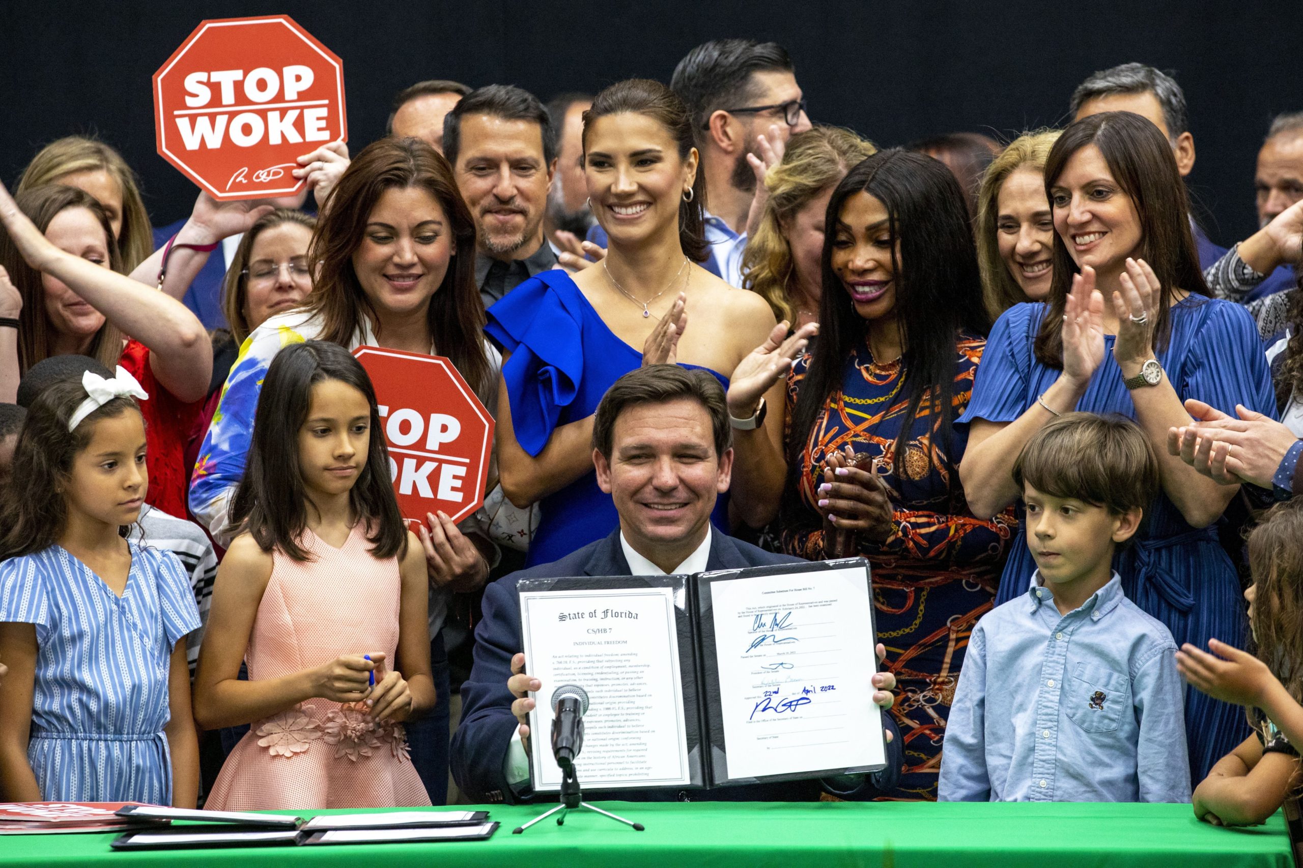 Florida Gov. Ron DeSantis signs the “Stop WOKE Act” publicly, surrounded by a group of supporters.