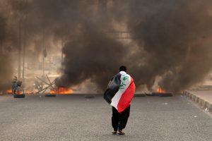 TOPSHOT - A supporter of Iraqi Shiite cleric Moqtada Sadr carries the Iraqi flag as he walks down a road blocked by burning tyres during a demonstration in Iraq's southern city of Basra on August 29, 2022. - Dozens of angry supporters of the powerful cleric stormed the Republican Palace, a ceremonial building in the fortified Green Zone, a security source said, shortly after Sadr said he was quitting politics. The army has announced a  Baghdad-wide curfew to start from 3:30 pm (1230 GMT). (Photo by Hussein Faleh / AFP) (Photo by HUSSEIN FALEH/AFP via Getty Images)